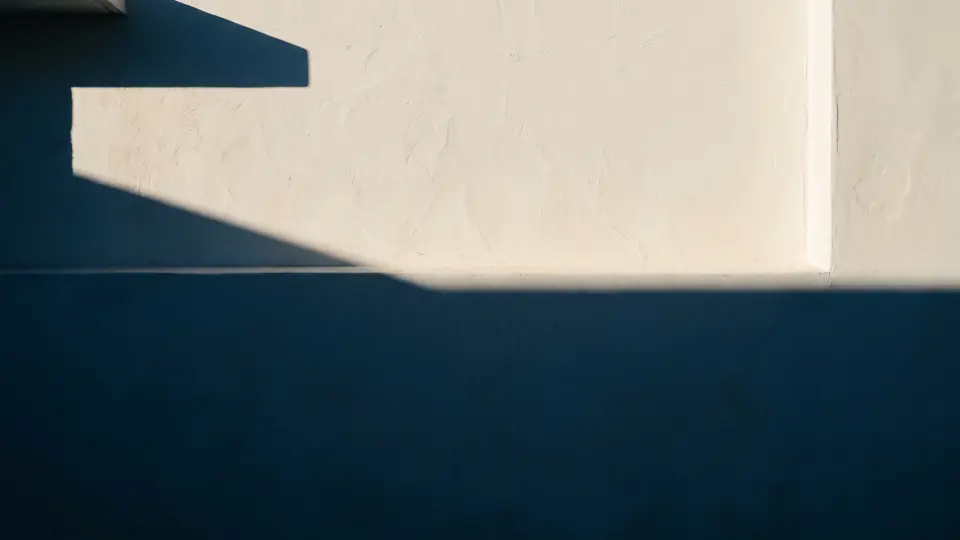 A plain interior wall in cream above a deep navy dado, with a diagonal band of afternoon light across it.